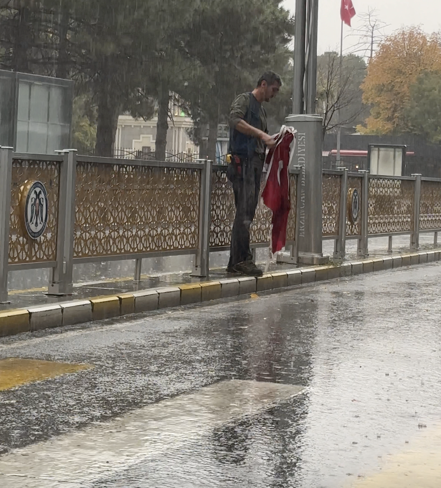 Yağmurda yere düşen bayrakları katlayıp aldı